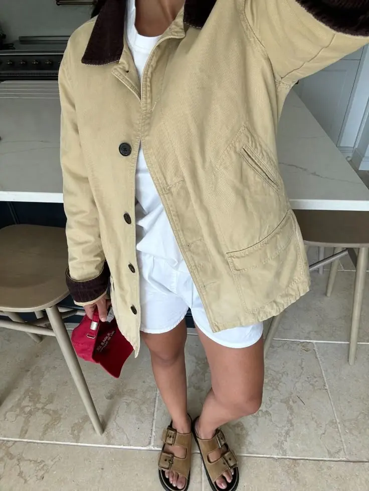 Beige barn jacket outfit with white button-down, brown shorts, and Birkenstock sandals for spring
