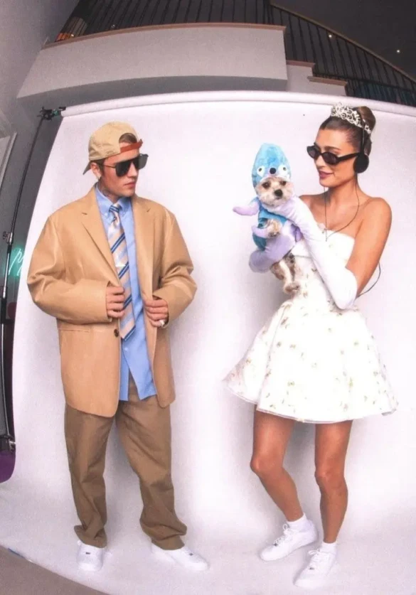man in tan suit with sunglasses and hat standing next to woman in white dress with tiara and small dog in blue costume outfit 1