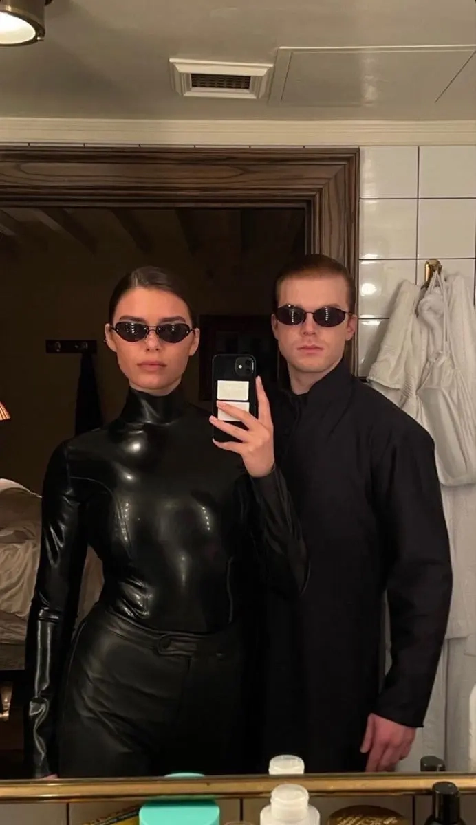 woman in black leather outfit next to man in black coat and sunglasses taking bathroom mirror selfie outfit 12