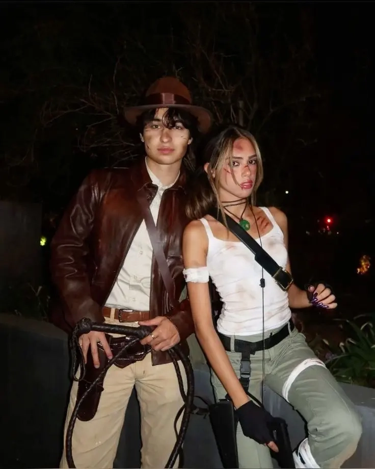 man in brown leather jacket and fedora with whip next to woman in beige tank top and tactical gear with weapons outfit 13