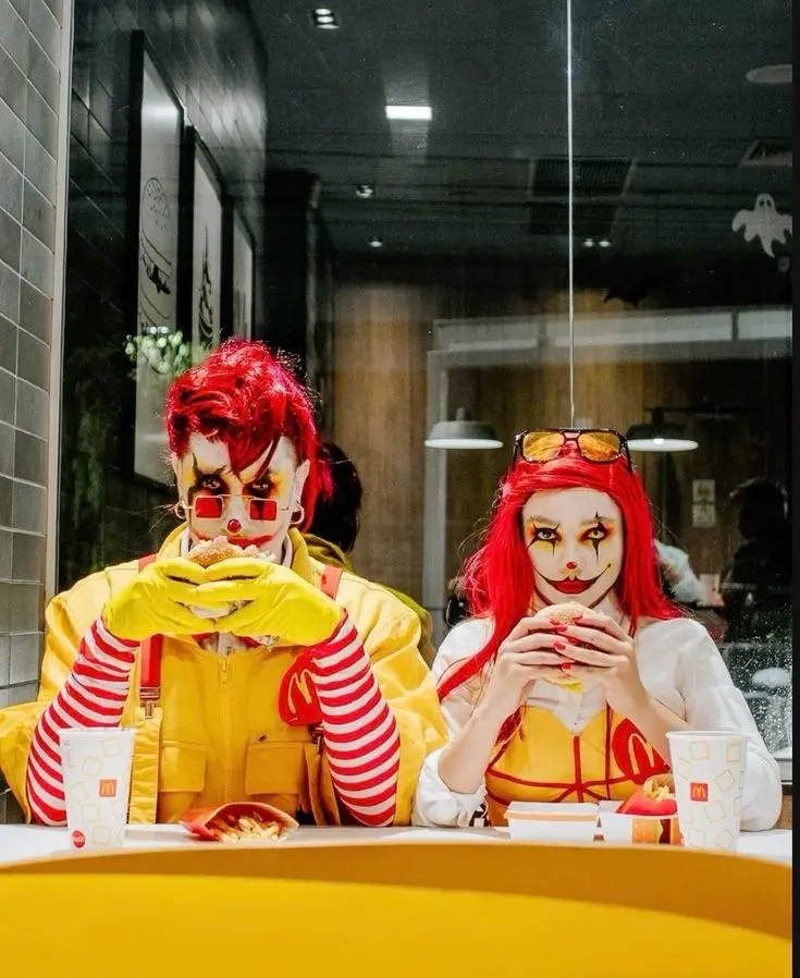 man in yellow mcdonald's uniform with red wig next to woman in similar outfit with red braided wig eating at table outfit 19