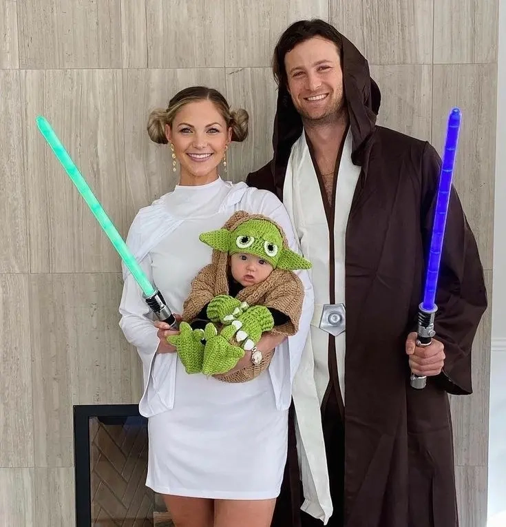 woman in princess leia costume white dress hair buns, man in jedi costume brown robes, baby in yoda costume green with ears star wars family outfits 5