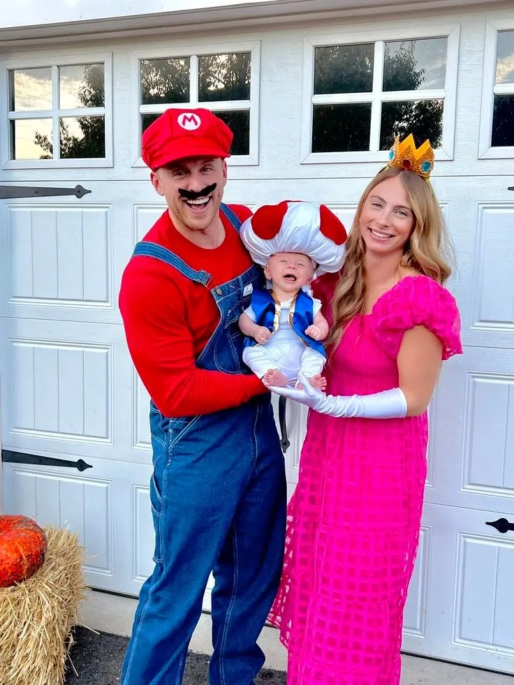 man in mario costume with red hat blue overalls, woman in pink princess dress with crown, baby in toad costume family halloween outfits 1