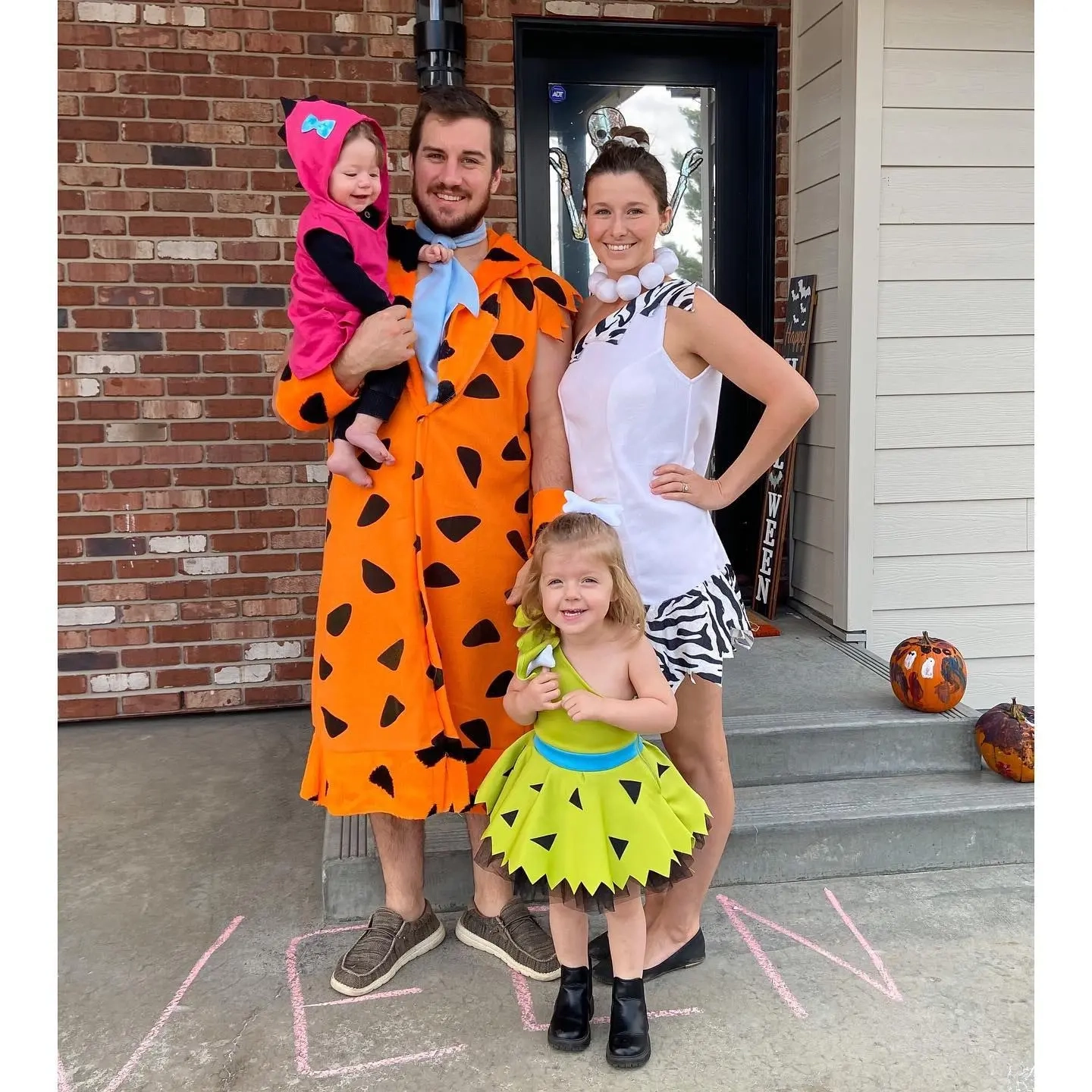 man in fred flintstone orange costume black spots, woman in wilma costume white dress, children in pebbles and bamm bamm costumes flintstones family outfits 7