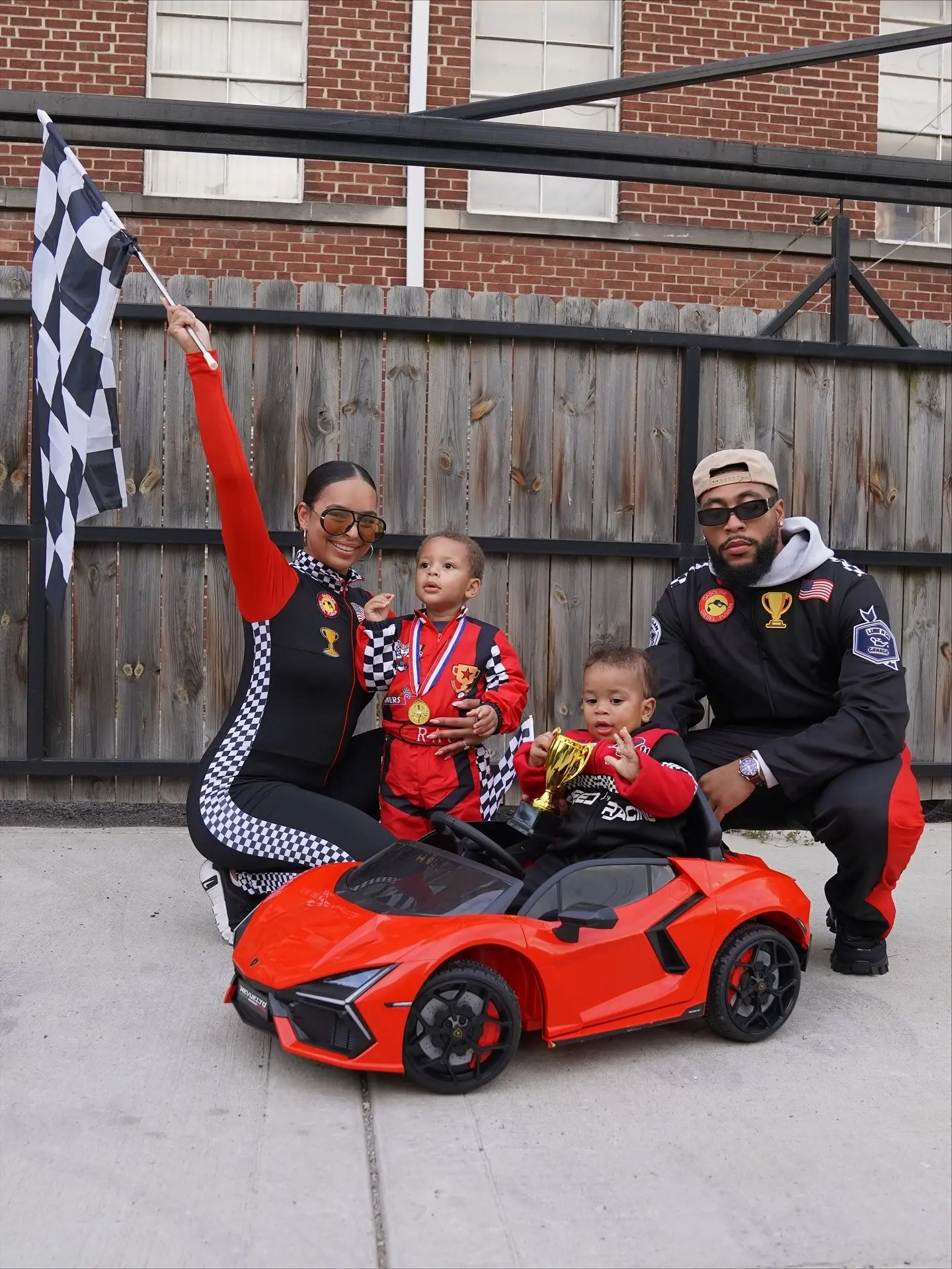 family in matching black racing suits with checkered pattern details, children and adults in race car driver costumes with red toy car racing family outfits 6