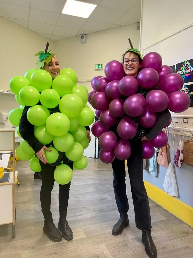 two women as grape clusters with green and purple balloons attached outfit 12