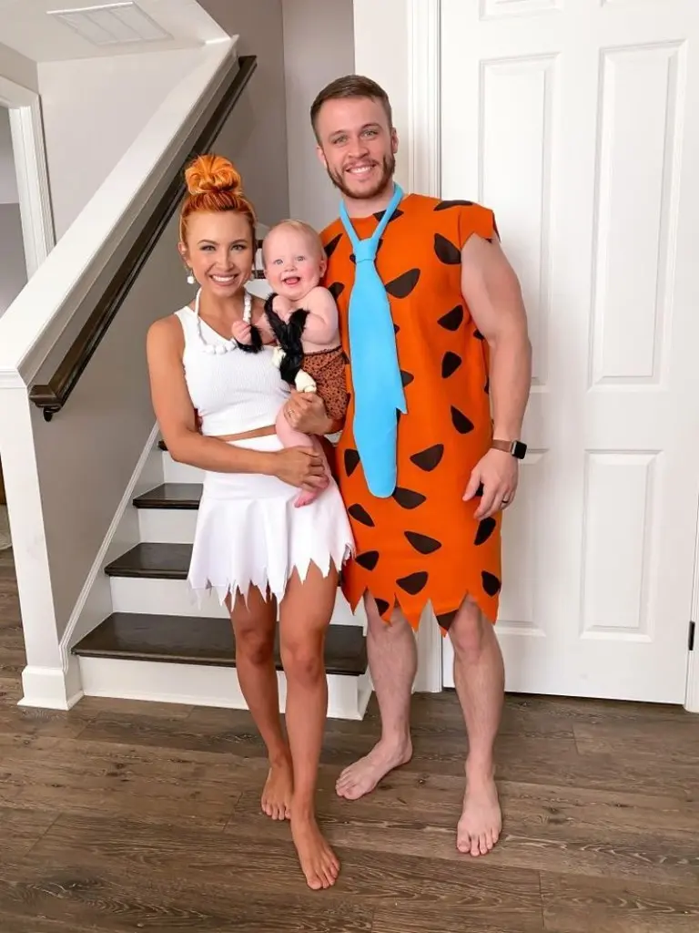 family of three in flintstones halloween costumes white dress orange spotted tunic blue tie baby caveman outfit 1