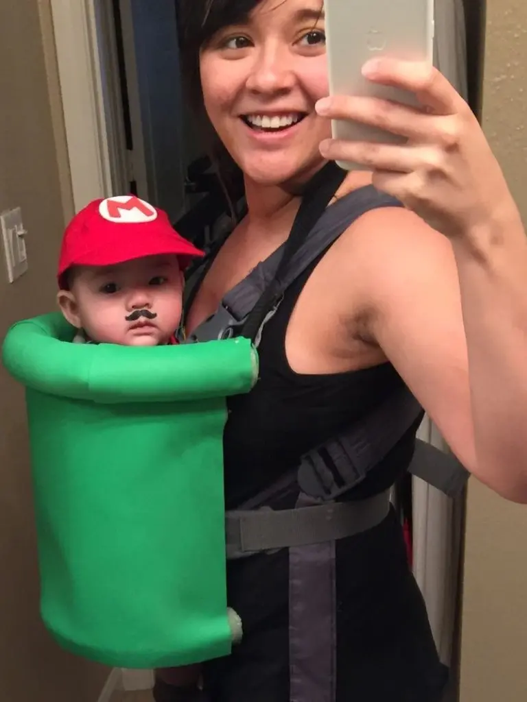 woman wearing baby in carrier dressed as mario pipe costume red hat mustache green tube around baby 11
