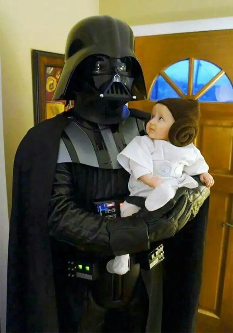 man in darth vader costume holding baby dressed as princess leia in white outfit with hair buns 12