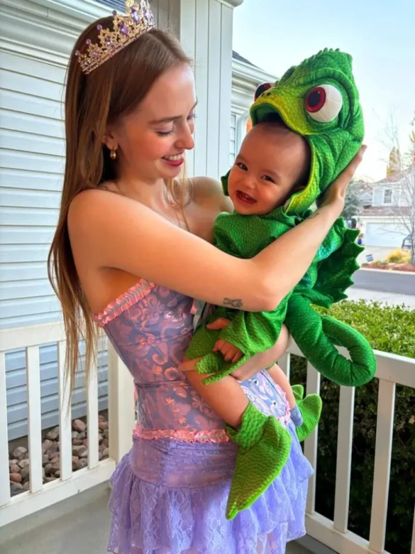 woman wearing purple dress and crown holding smiling baby in green chameleon costume 15