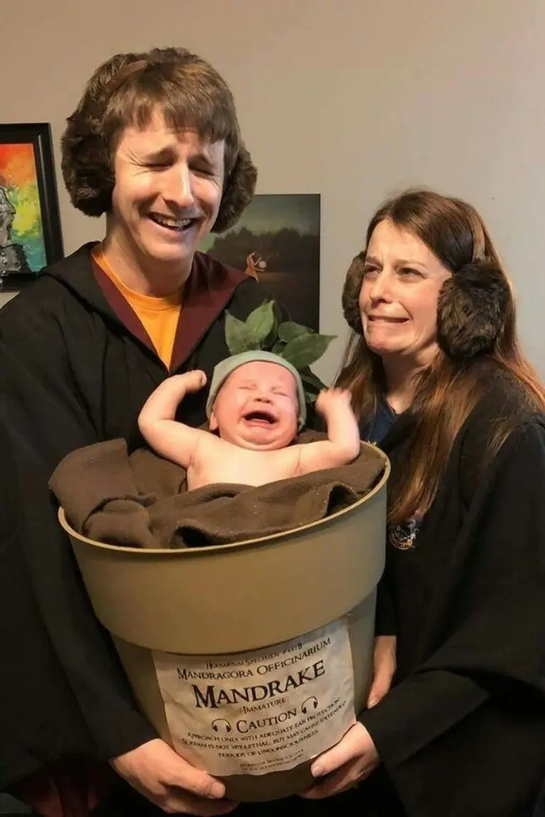 family in dark robes holding crying baby in brown mandrake plant costume pot 18