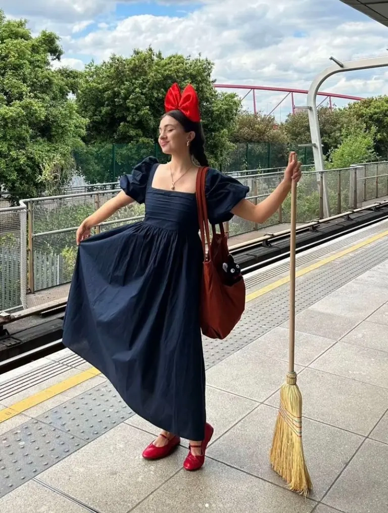 teenage girl wearing kiki delivery service costume navy dress red bow broom prop outfit 11