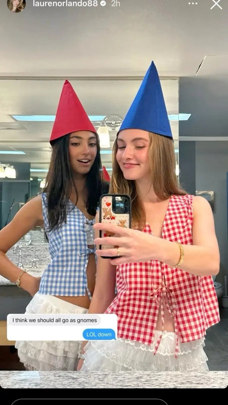 two teenage girls wearing red and blue pointed gnome hats with gingham tops white skirts taking selfie outfit 1