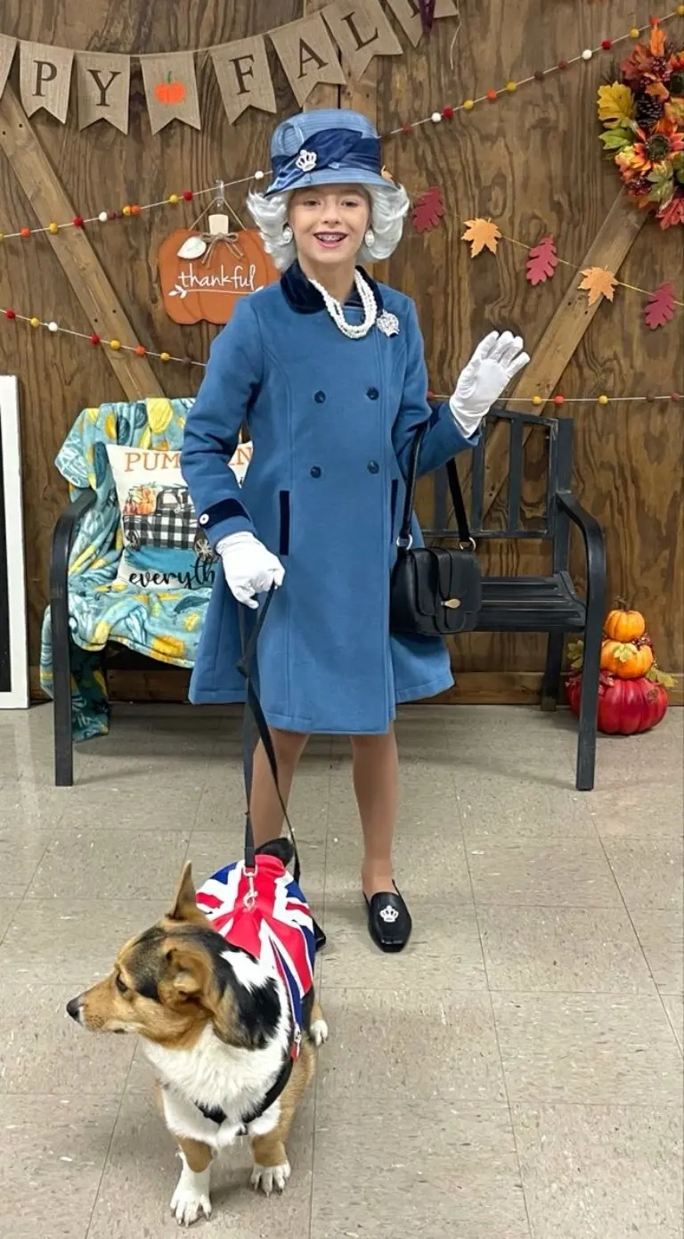 teenage girl wearing queen elizabeth ii costume blue coat pearls hat british flag prop corgi outfit 12