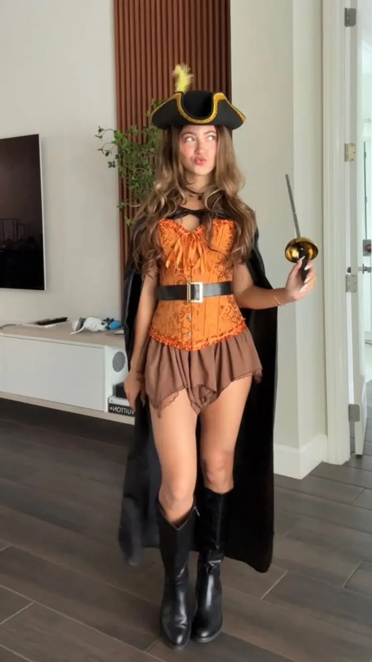 woman wearing orange corset brown shorts pirate hat and black boots with cape costume outfit 7
