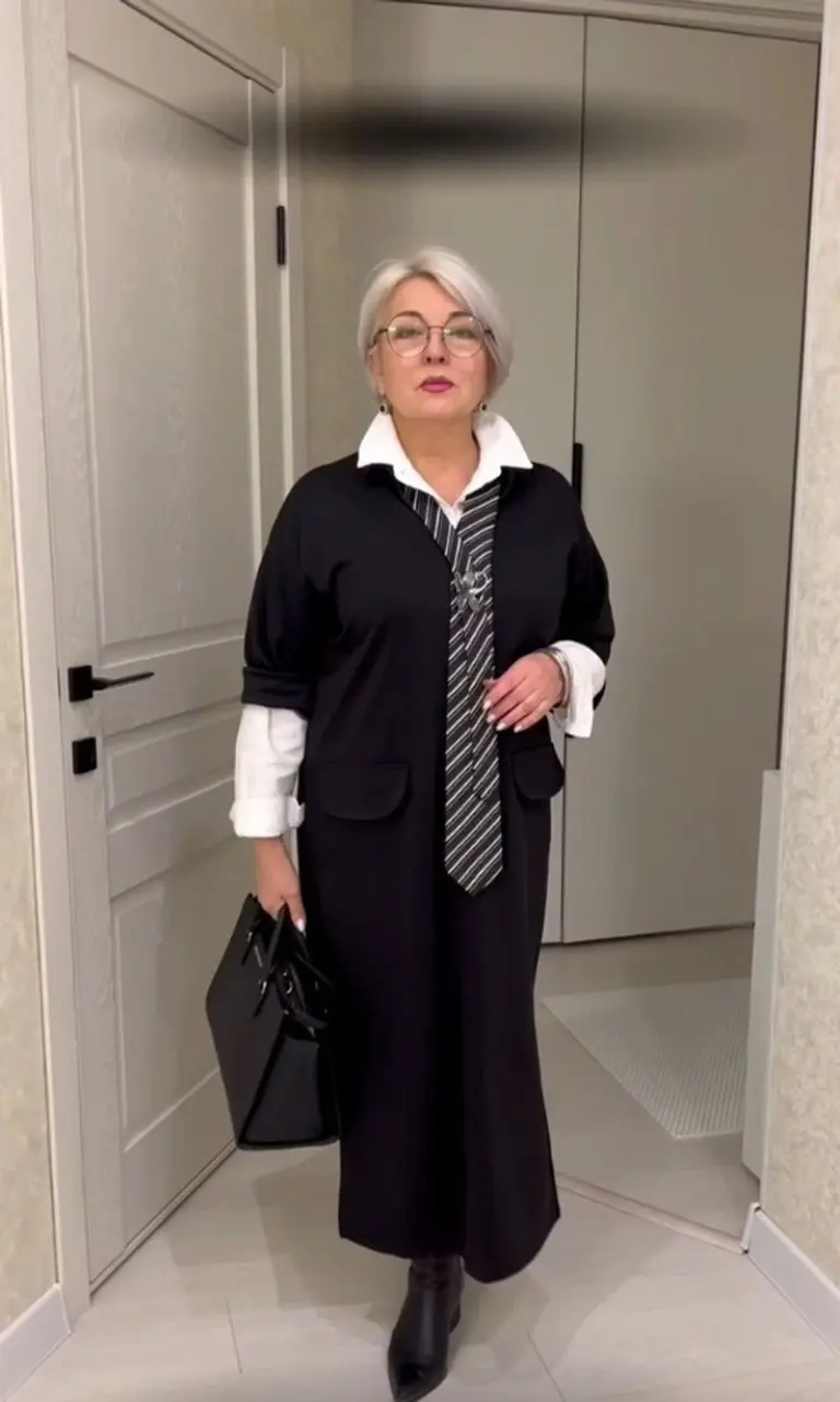 woman in black cardigan white shirt striped tie long black coat structured bag ankle boots 5