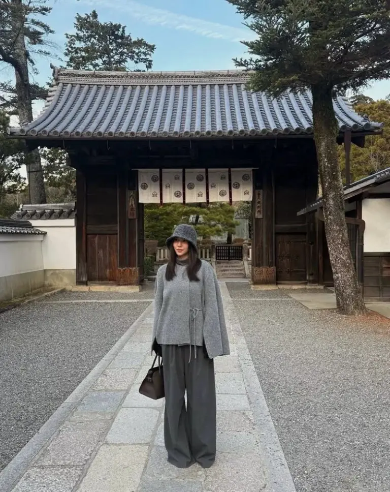 woman in grey wool cape bucket hat wide leg trousers black handbag traditional temple background outfit 6