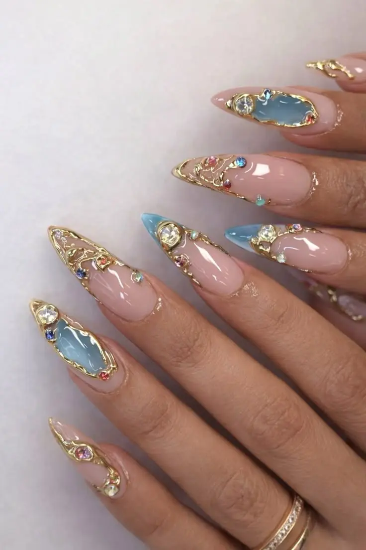 medium long stiletto nude pink nails with gold filigree lines blue opaque accent stones and scattered small colored rhinestones photo 4