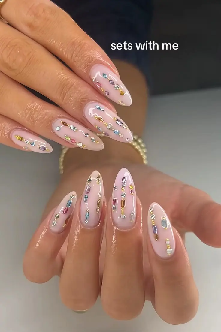 sheer pink milky almond nails with vertical cascading mixed baguette and round gems in rainbow colors and gold micro-beads photo 6