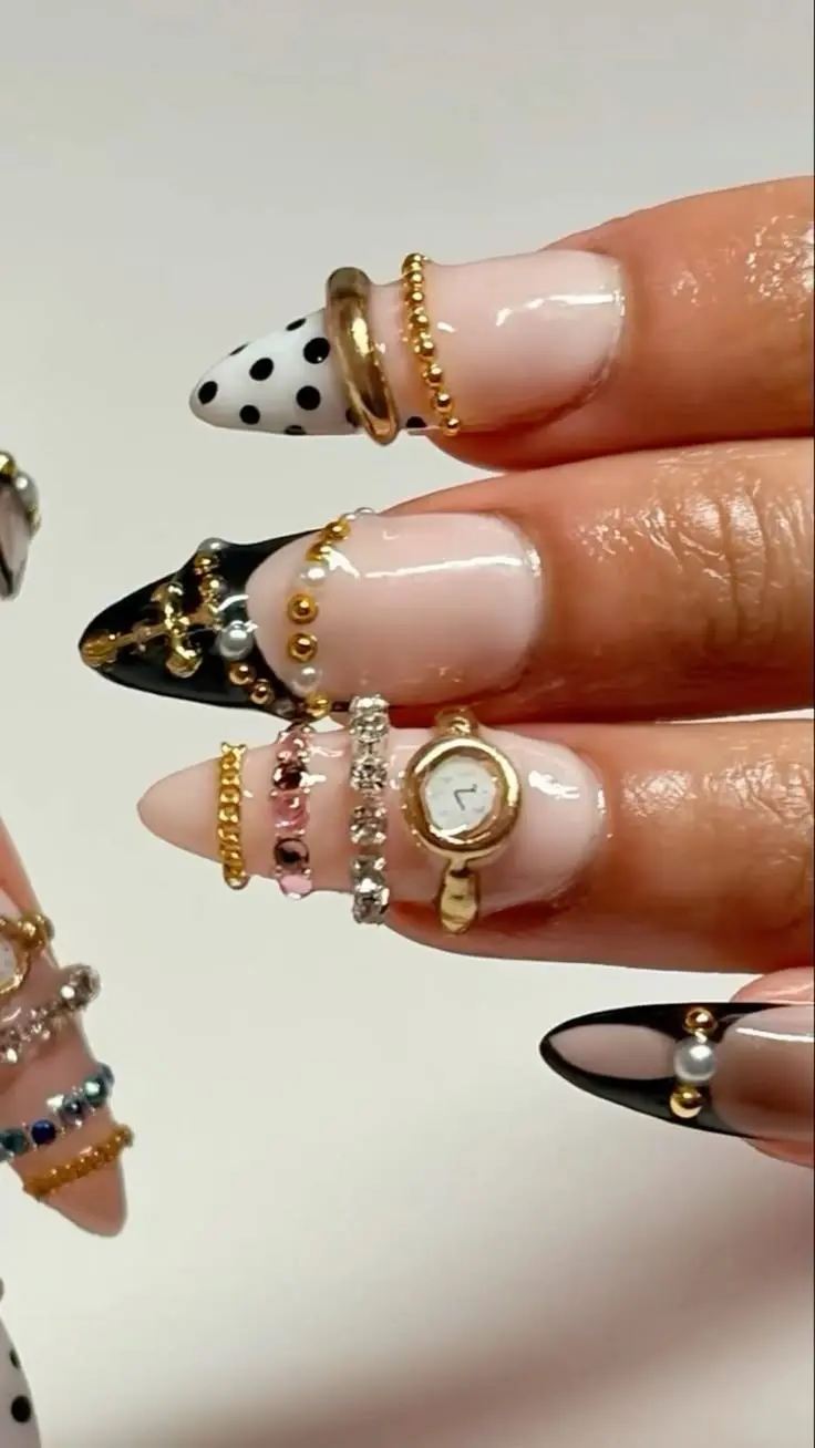 stiletto nails with black gel tips white polka dot accent nude base and stacked gold bead crystal and pink gem nail ring charms with miniature watch charm photo 10