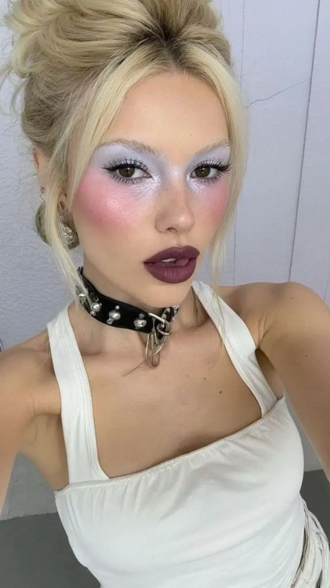 blonde woman with lavender glitter eyeshadow blush on nose and cheeks dark burgundy lip and updo hairstyle cold girl makeup look 1