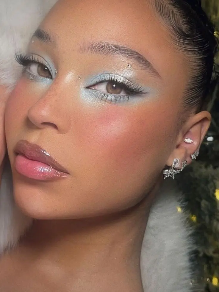woman with ice blue eyeshadow black liner wing rhinestones inner corner pink gloss lip high blush on cheeks and nose cold girl makeup look 3