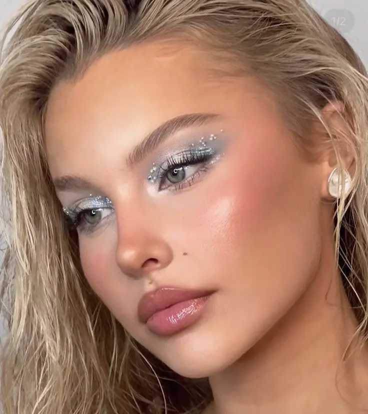 blonde woman with silver glitter halo eyeshadow scattered gems brow area warm pink blush glazed nude lip cold girl makeup look 4