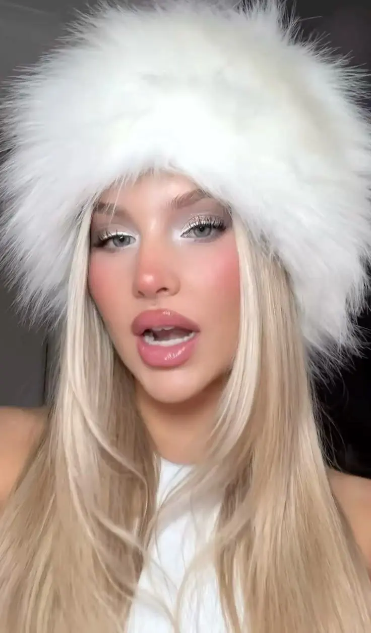 blonde woman wearing white fluffy hat silver shimmer eyeshadow pink blush on nose and cheeks glossy pink lip cold girl makeup look 7