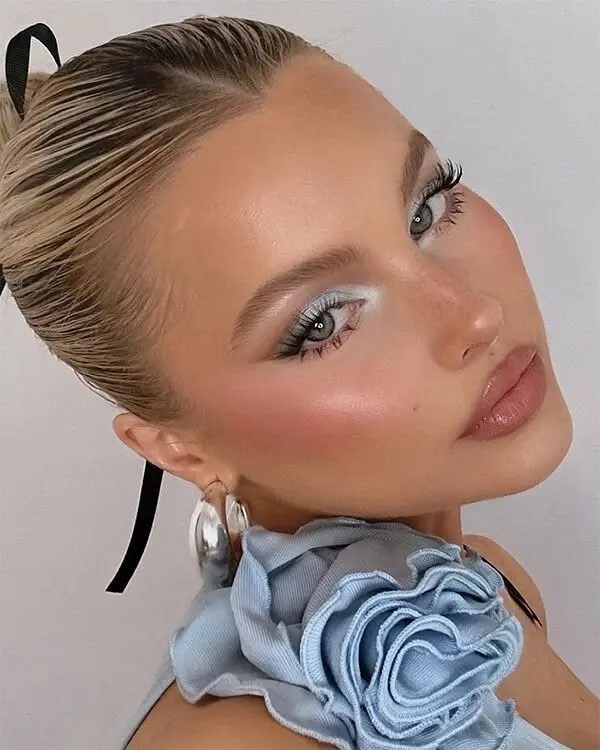blonde woman slicked back bun pale ice blue eyeshadow short liner wing rosy blush peachy glow skin nude rose gloss lip silver hoop earrings cold girl makeup look 9