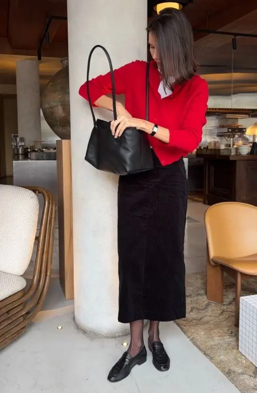 woman in red fine knit cardigan white shirt black corduroy midi skirt sheer black tights black leather loafers black shoulder tote bag fall work outfit 8