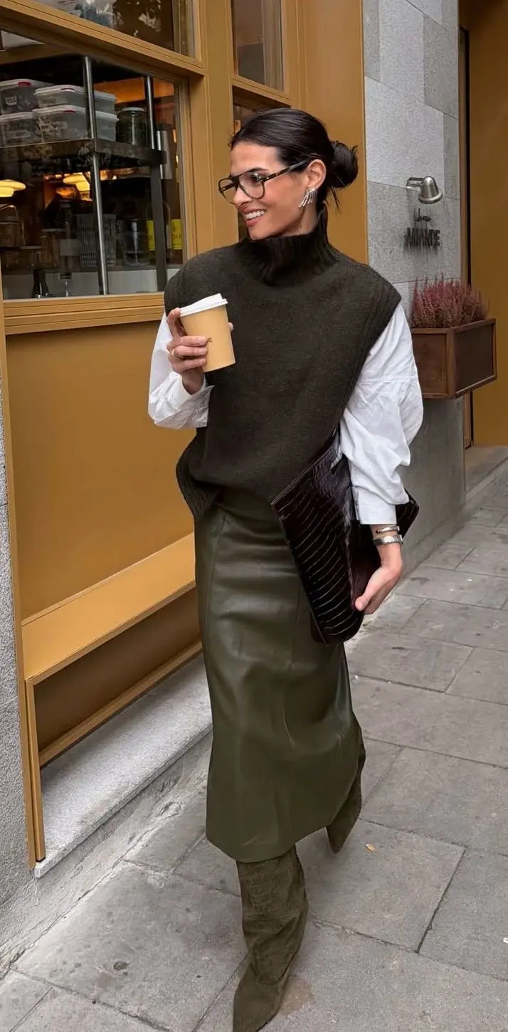 woman in dark olive turtleneck sweater vest white oversized shirt olive leather midi skirt dark brown croc clutch olive suede knee high boots glasses hair up fall work outfit 11