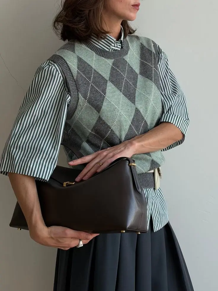 woman in argyle sweater vest green grey over striped green white oversized shirt dark navy pleated midi skirt dark brown structured leather bag fall work outfit 12
