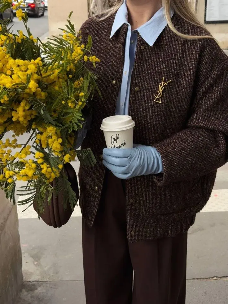 woman in brown tweed bomber jacket sky blue collar shirt dark brown wide trousers pale blue leather gloves brown shoulder bag coffee cup flowers street fall work outfit 13