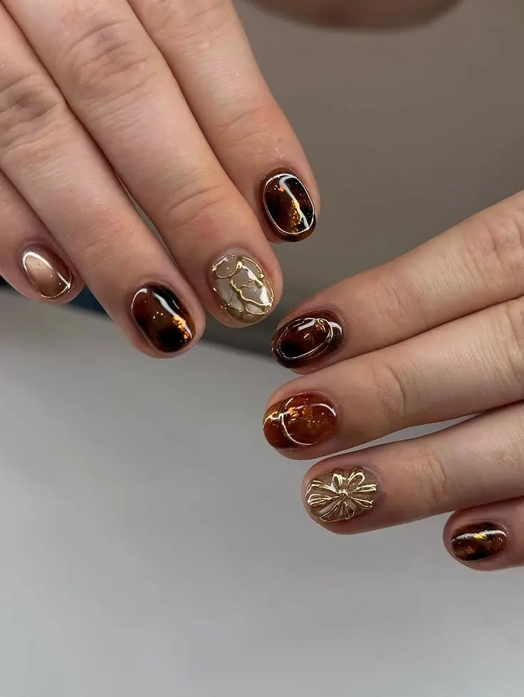 short oval nails with dark brown tortoiseshell base gold foil accents 3D cream and gold floral nail art on one finger photo 1