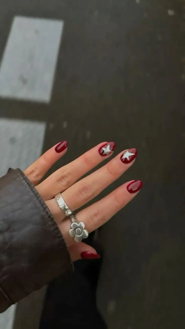 short oval nails deep burgundy red gel with silver star accents on two nails one outlined one solid photo 13