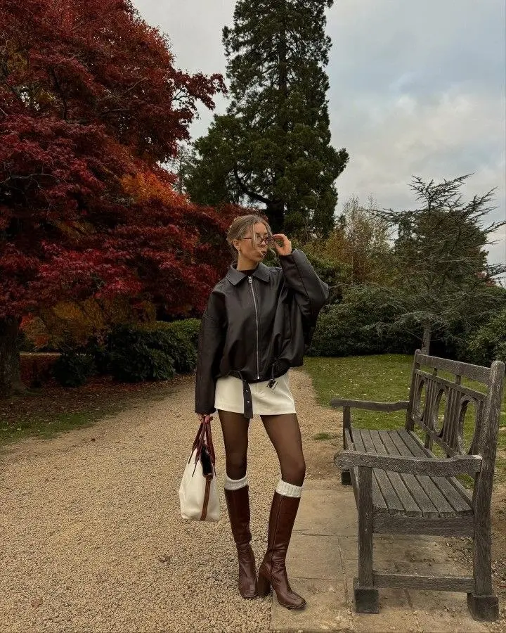woman in oversized dark leather jacket cream mini skirt black tights knee high brown boots white canvas tote bag autumn park pumpkin patch outfit 2