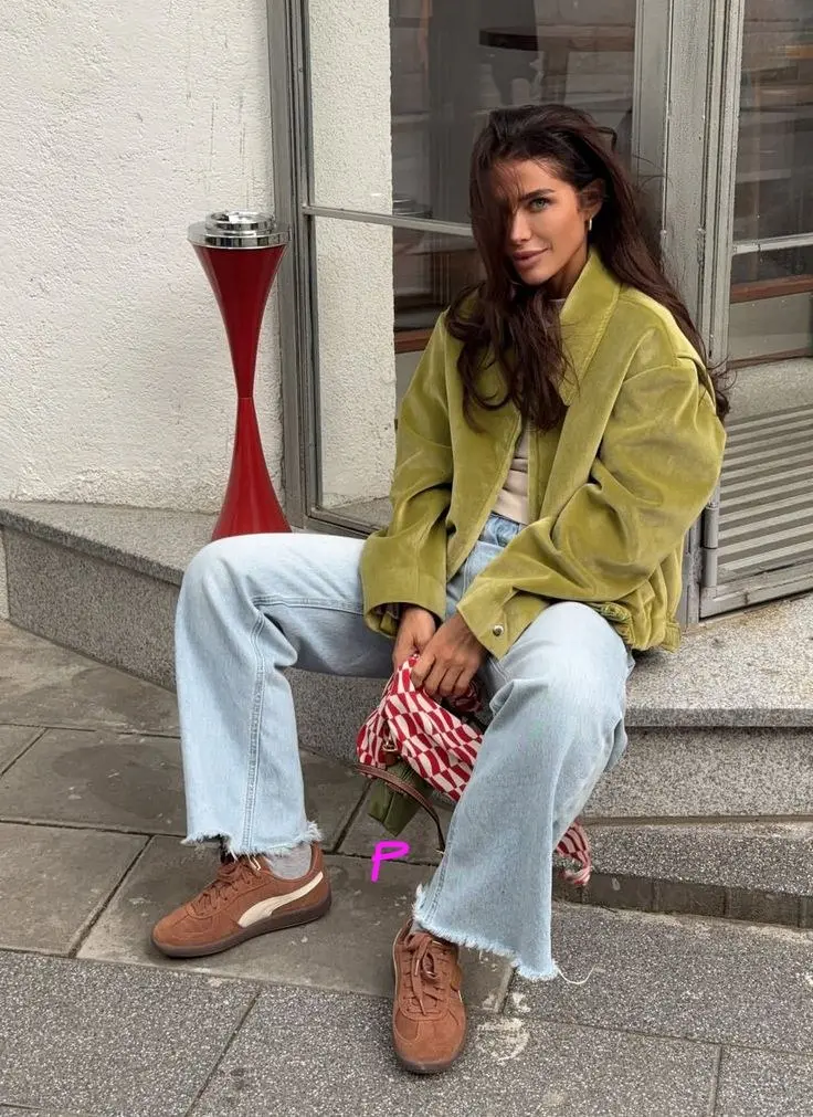 woman sitting on steps in olive green oversized corduroy jacket light wash straight leg jeans brown suede sneakers red striped mini bag pumpkin patch outfit 3