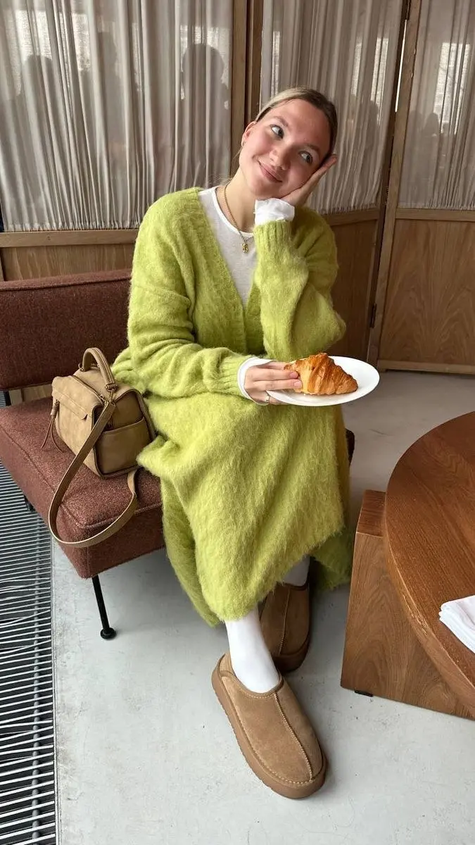 woman sitting indoors in lime green longline mohair cardigan white tee dress white ribbed tights platform UGG slippers tan suede mini backpack croissant pumpkin patch outfit 7