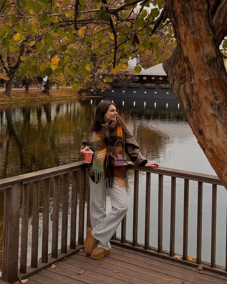 woman standing by lake railing in plaid oversized mohair scarf grey wool jacket light wide leg trousers platform boots small dark structured bag autumn foliage pumpkin patch outfit 8