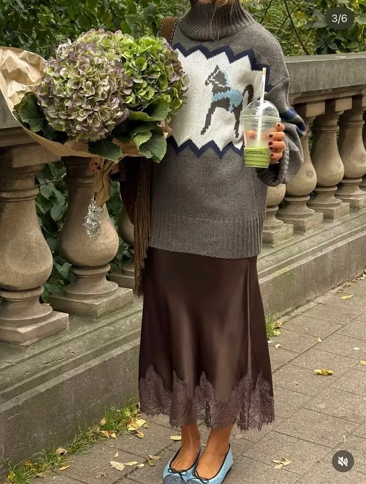 woman outdoors holding flowers in grey intarsia turtleneck sweater tucked into chocolate satin midi skirt lace hem blue ballet flats fringe bag pumpkin patch outfit 10