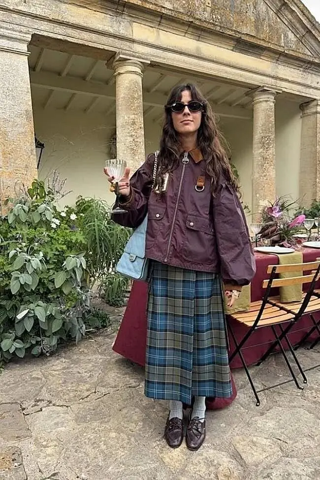 woman standing at outdoor stone venue in burgundy utility jacket teal green tartan midi skirt grey ribbed socks dark brown oxford shoes blue shoulder bag pumpkin patch outfit 11