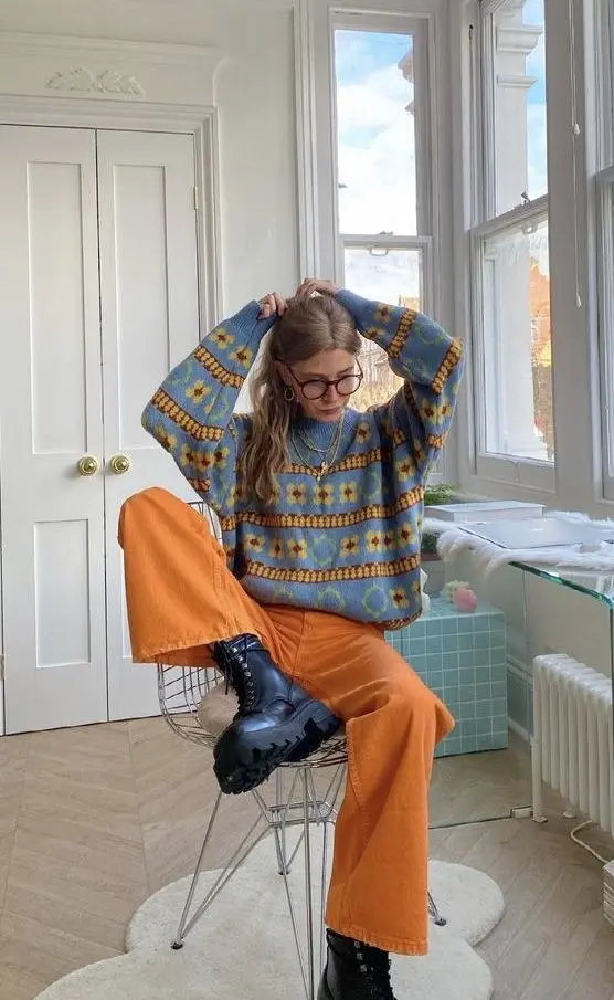 woman seated indoors in blue floral intarsia knit sweater rust orange wide leg corduroy trousers black chunky lace up boots layered necklaces pumpkin patch outfit 12