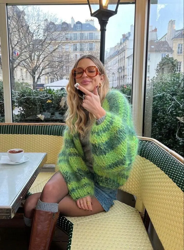 woman seated at cafe table in oversized green striped mohair sweater denim micro-skirt knee high brown leather boots tortoiseshell glasses pumpkin patch outfit 13