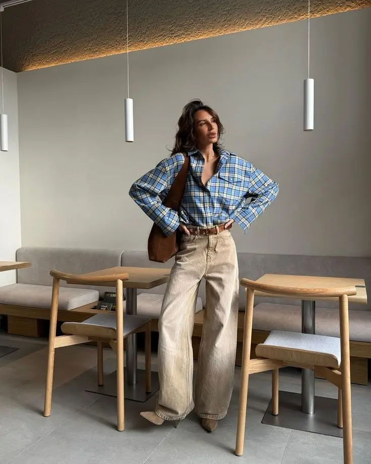 woman standing in modern cafe interior in blue yellow plaid flannel shirt sand wide leg jeans brown leather belt tan suede shoulder bag cowboy toe ankle boots pumpkin patch outfit 16