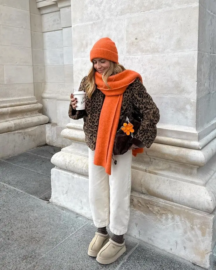 woman leaning on stone wall in leopard print faux fur teddy coat orange beanie orange scarf white straight leg jeans platform UGG boots small brown fur bag pumpkin patch outfit 17