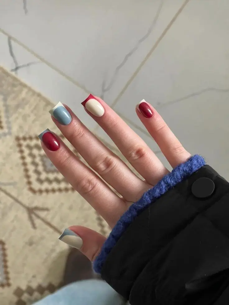 short square nails with color block French design in burgundy, dusty blue-grey, and cream-white, mixed per finger, hand in black jacket with blue cuff, photo 7