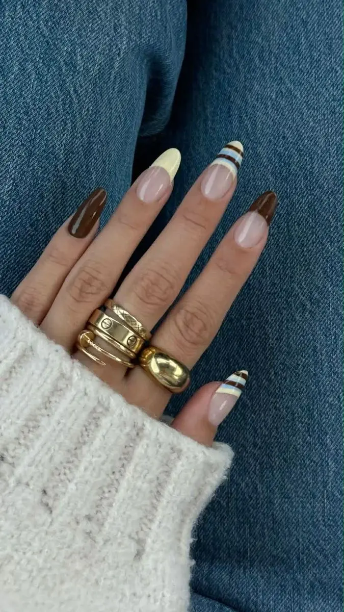 long almond nails with sheer nude base, cream French tips, solid chocolate brown nails, and one accent nail with brown and blue horizontal pinstripes, photo 3