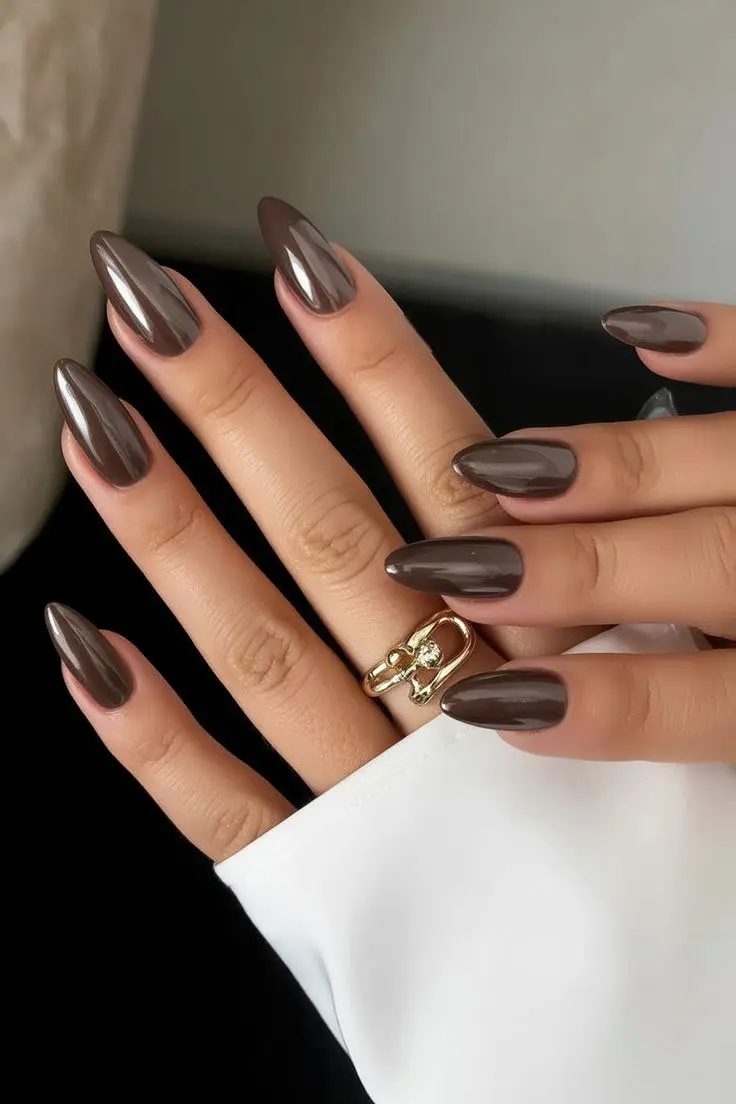 medium-long almond nails in deep warm espresso brown with soft chrome pearl finish at high gloss, gold sculptural ring, white cuff background, photo 15