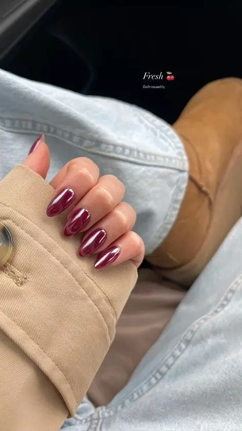 short almond nails in glossy cherry-burgundy warm wine-red gel polish with domed high-gloss finish, held against light denim, photo 20