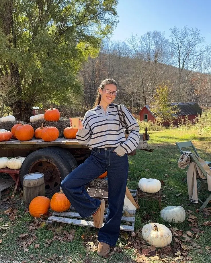 woman in navy cream breton stripe polo sweater dark indigo wide leg jeans camel mules and small shoulder bag at outdoor pumpkin farm with hay bales outfit 5